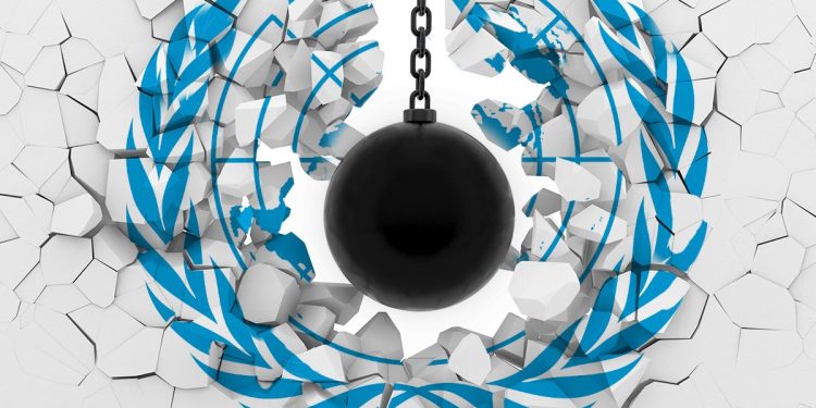 A wrecking ball knocking down a white wall displaying a United Nations logo