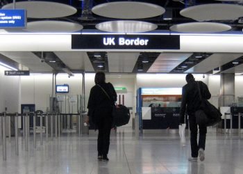Two peaople in dark clothes and hoodies walking toward the UK Border customs area at Heathrow airport
