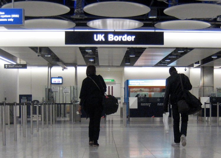 Two peaople in dark clothes and hoodies walking toward the UK Border customs area at Heathrow airport