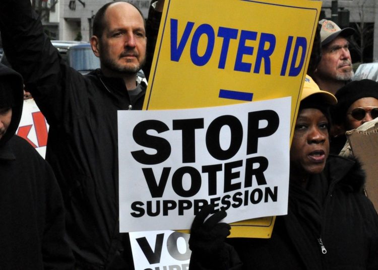 People demonstrating holding placards saying 'stop voter suppression' and 'voter ID'