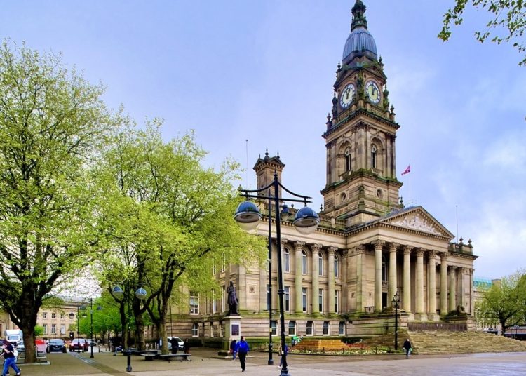 large majestic building with pillars on the front and a high tower, and two trees next to it.