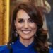 Kate Middleton smiling at the camera. she wears blue clothes and has long brown waving hair