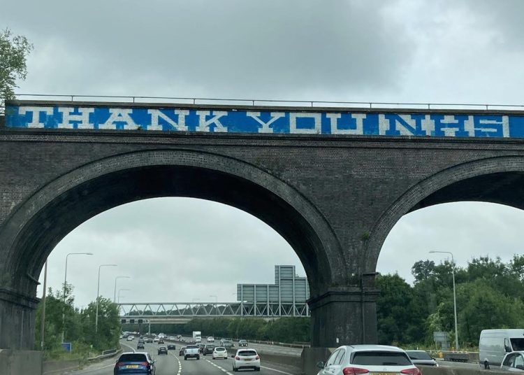 A viaduct over a road, and a large blue banner saying Thank you NHS in white letters on the side of the viaduct