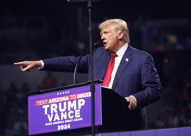 Man in a suit stands behind a pedestal, and points his right hand