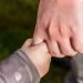 Close up of a young child's hand holding on to the index finger of a man as if they are walking away from the camera together.