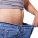 Woman wearing a pair of jeans that are too big for her she is holding them out away from her body
