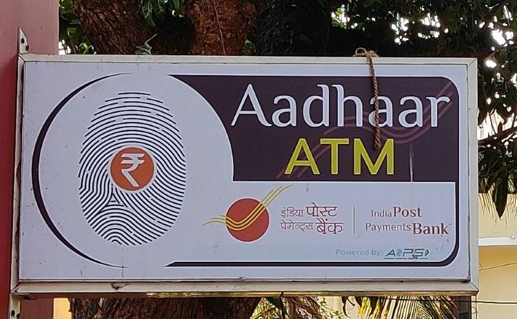 sign on the side of a building in India that reads "Aadhaar ATM" there is a fingerprint image on the sign as well