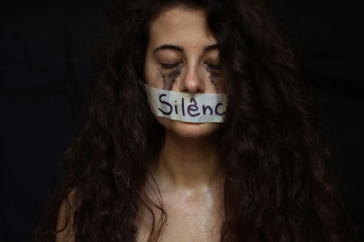 woman with tape across her mouth on the tape is written Silenci